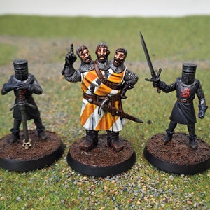 Può includere: Tre figure in miniatura dipinte di cavalieri, una con tre teste, in piedi su basi circolari. Il cavaliere con tre teste indossa un'armatura gialla e bianca, mentre gli altri due cavalieri indossano un'armatura nera.