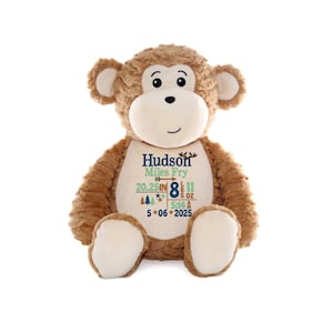 May include: A plush monkey with brown fur and a cream-colored face, hands, and feet. The monkey has embroidered details and a personalized design on its chest with the name "Hudson Miles Fry", measurements, and date.