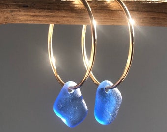 May include: Gold hoop earrings with blue sea glass charms. The earrings are simple and elegant, perfect for everyday wear.