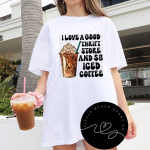Puede incluir: Camiseta blanca con un dise&ntilde;o gr&aacute;fico de una taza de caf&eacute; helado y el texto "Me encanta una buena tienda de segunda mano y caf&eacute; helado de 8 euros".