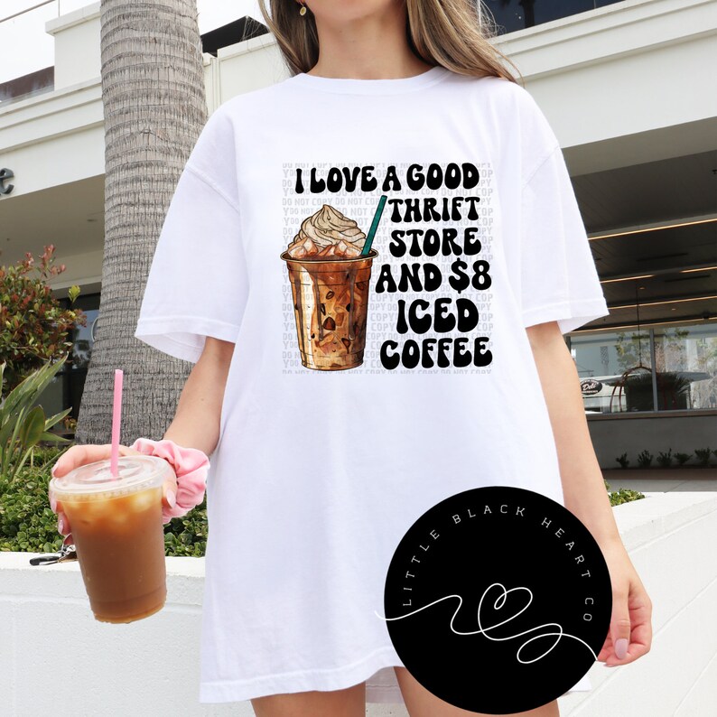 Puede incluir: Camiseta blanca con un dise&ntilde;o gr&aacute;fico de una taza de caf&eacute; helado y el texto "Me encanta una buena tienda de segunda mano y caf&eacute; helado de 8 euros".