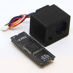 Op de afbeelding: Een zwarte printplaat met de tekst "WLA82" en "XILINX" erop gedrukt. Een zwarte 3D-geprinte doos met een connector aan de zijkant en een kabel met een witte connector aan het andere uiteinde.