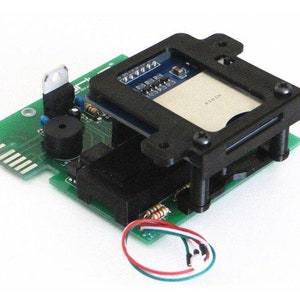 Op de afbeelding: Een groene printplaat met diverse elektronische componenten, waaronder een zwart rechthoekig frame, een kleine luidspreker en een meerkleurige draad. Het frame bevat een kleine kaart. De componenten zijn op de printplaat geplaatst.