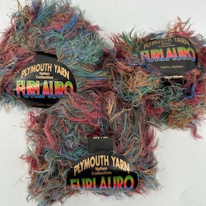Może przedstawiać: Trzy motki przędzy Plymouth Yarn Furlauro Italian Collection. Przędza jest mieszanką kolorów, w tym czerwonego, niebieskiego, zielonego i brązowego. Każdy motek ma etykietę z napisem "Furlauro" i "100% Nylon".