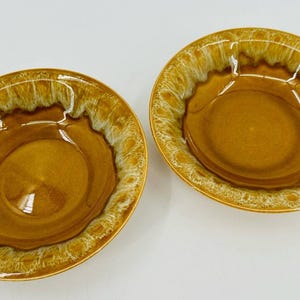 May include: Two ceramic bowls with a brown glaze and a white and brown textured rim. The bowls have a circular shape and are set against a white background. The bowls are likely for serving food.