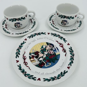 May include: A white ceramic dinnerware set featuring two cups with matching saucers and one large plate. The pieces are decorated with green holly, red berries, and Mickey Mouse motifs. The text reads, "Twas the night before Christmas and all through the house... and to all a good night."
