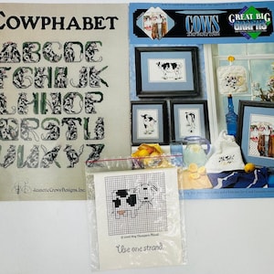 May include: A cross-stitch pattern booklet featuring a cow alphabet, titled "Cowphabet". The booklet includes a variety of cow-themed cross-stitch patterns, including a cow alphabet, a cow in a kitchen, and a cow in a field. The booklet also includes a small, separate cross-stitch pattern for a single cow.