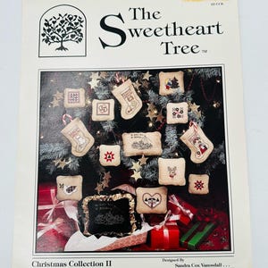 May include: A Christmas Collection II pattern book featuring cross-stitch designs. The cover displays various small, embroidered Christmas ornaments, including stockings, stars, and squares, arranged against a backdrop of a Christmas tree and gifts.