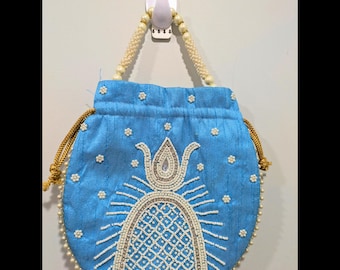 May include: A light blue drawstring bag with a beaded design. The bag features a central beaded motif and is adorned with small, white floral embellishments. The handles are made of cream-colored beads. The bag is hanging on a white hook.