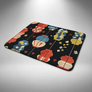 May include: A black rectangular mouse mat with a repeating pattern of red, yellow, and blue stylized lanterns. Small white flowers and red accents are scattered across the surface. The design has a vintage, artistic aesthetic.