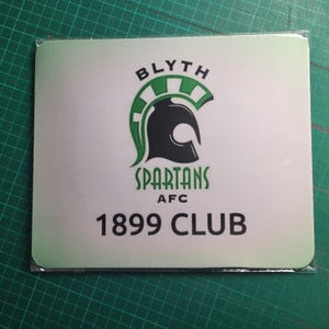 May include: Square mousepad with the Blyth Spartans AFC logo. The logo features a black Spartan helmet with green accents, the word "SPARTANS" and "1899 CLUB" in black text. The background is white with a green gradient.