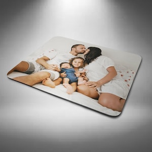 May include: Rectangular mouse mat featuring a family portrait. The image shows a family of four, with the parents kissing and two children. The mouse mat has a black border and is on a white background.