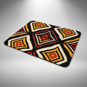 May include: Rectangular black mouse mat with a repeating geometric pattern. The design features squares in shades of red, yellow, and cream, outlined in black. The pattern is reminiscent of tribal art.