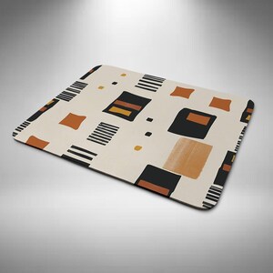 May include: Rectangular beige mouse mat with a geometric pattern. The design features black, brown, and orange shapes, including squares, rectangles, and stripes. The mouse mat has rounded corners and a smooth surface.
