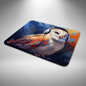 May include: Square mouse mat featuring a stylized illustration of a white owl wearing headphones. The owl has orange and brown feathers, set against a blue and orange background. The mouse mat is designed for computer use.