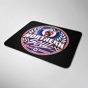 May include: A rectangular black mouse mat featuring a circular graphic with the text NORTHERN SOUL. The design includes a dancing figure, a red, white, and blue target emblem, laurel leaf accents, and a black and white checkered pattern border.