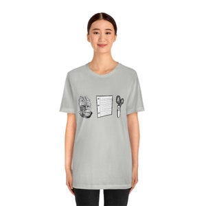 以下が含まれることがあります： 薄いグレーのTシャツに、黒と白の生き物の頭、線が入った紙、ハサミのイラストが描かれています。