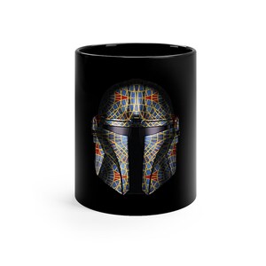 May include: A black ceramic mug with a geometric design of a Mandalorian helmet in blue, yellow, and red.