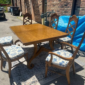 May include: A wooden dining table set with four chairs. The table has a brown wood top and a carved base. The chairs have a brown wood frame and a white and blue floral patterned fabric seat.