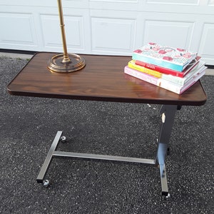 May include: A brown wooden table with a silver metal frame and wheels. The table has a stack of cookbooks on top, including "Salads" and "The Conscious Cook".