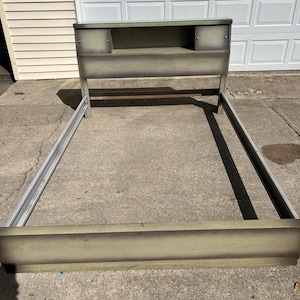 May include: A vintage bed frame with a headboard featuring a built-in shelf and two small cubbies. The frame and headboard have a distressed, faded green and gray finish. The bed frame is made of wood and metal.