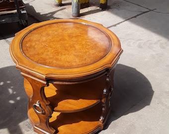 May include: A round wooden end table with two shelves and decorative metal ring pulls. The table has a rich brown wood grain finish.