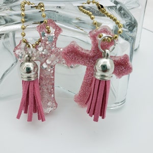 May include: Two pink glitter cross charms with gold chains and pink tassels.