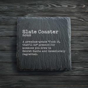 Peut inclure: Un dessous de verre carré en ardoise avec le texte "Slate Coaster noun" et une définition humoristique. La définition se lit comme suit : "Un cadeau 'fuck it, that'll do' de qualité supérieure pour quelqu'un que vous avez dessiné au Secret Santa et que vous avez immédiatement regretté."