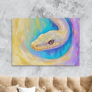Puede incluir: Impresión en lienzo que representa una serpiente estilizada en tonos amarillos, azules y morados. La cabeza de la serpiente está en el centro, con su cuerpo formando una espiral. La obra de arte se exhibe sobre un sofá beige.