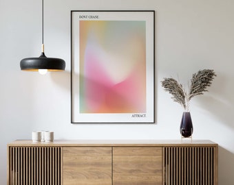 May include: A black pendant light hangs above a wooden cabinet with two doors. A framed poster with a blurred, colorful background and the text "DON'T CHASE. ATTRACT." is hanging on the wall behind the cabinet. A vase with dried pampas grass is on the cabinet.