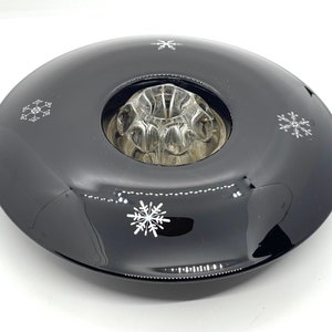 May include: A black glass candle holder with a snowflake design. The holder has a clear glass insert for a candle.
