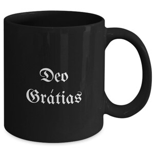 May include: Black ceramic coffee mug with white text that reads "Deo Gratias".