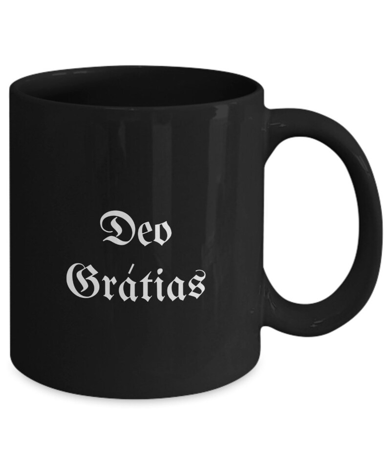 May include: Black ceramic coffee mug with white text that reads "Deo Gratias".