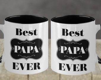 Puede incluir: Dos tazas de cerámica blanca con asas negras y bordes negros. Las tazas tienen un diseño en blanco y negro que dice "Best Papa Ever".