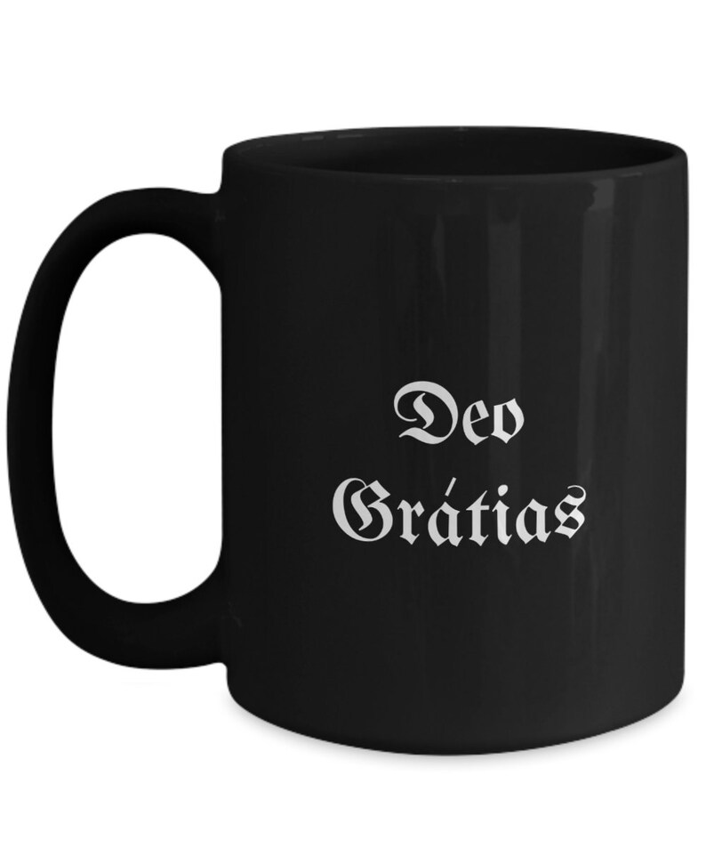 May include: Black ceramic coffee mug with white text that reads "Deo Gratias".