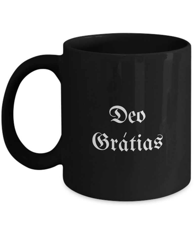 May include: Black ceramic coffee mug with white text that reads "Deo Gratias".