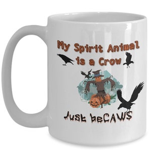 Puede incluir: Taza de caf&eacute; de cer&aacute;mica blanca con una ilustraci&oacute;n en negro y marr&oacute;n de un espantap&aacute;jaros con cuervos y calabazas. El texto en la taza dice "My Spirit Animal is a Crow Just because".