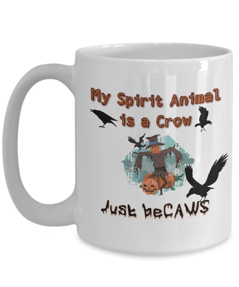 Puede incluir: Taza de caf&eacute; de cer&aacute;mica blanca con una ilustraci&oacute;n en negro y marr&oacute;n de un espantap&aacute;jaros con cuervos y calabazas. El texto en la taza dice "My Spirit Animal is a Crow Just because".