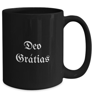 May include: Black ceramic coffee mug with a white inscription that reads "Deo Gratias".