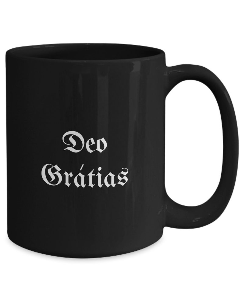 May include: Black ceramic coffee mug with a white inscription that reads "Deo Gratias".