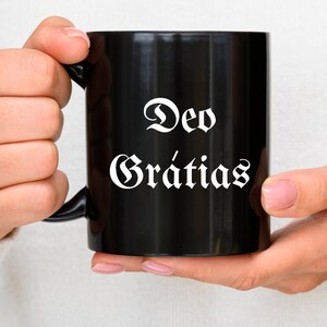 May include: A black ceramic mug with a white inscription that reads "Deo Gratias" in a gothic font.