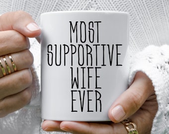 Puede incluir: Taza de cerámica blanca con texto negro que dice "Most Supportive Wife Ever".