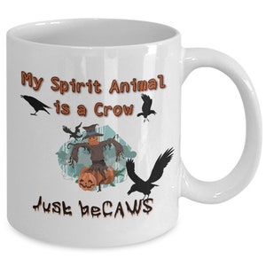 Puede incluir: Taza de caf&eacute; de cer&aacute;mica blanca con un dise&ntilde;o negro y naranja. La taza presenta un espantap&aacute;jaros con calabazas y cuervos. El texto en la taza dice "My Spirit Animal is a Crow Just Because".