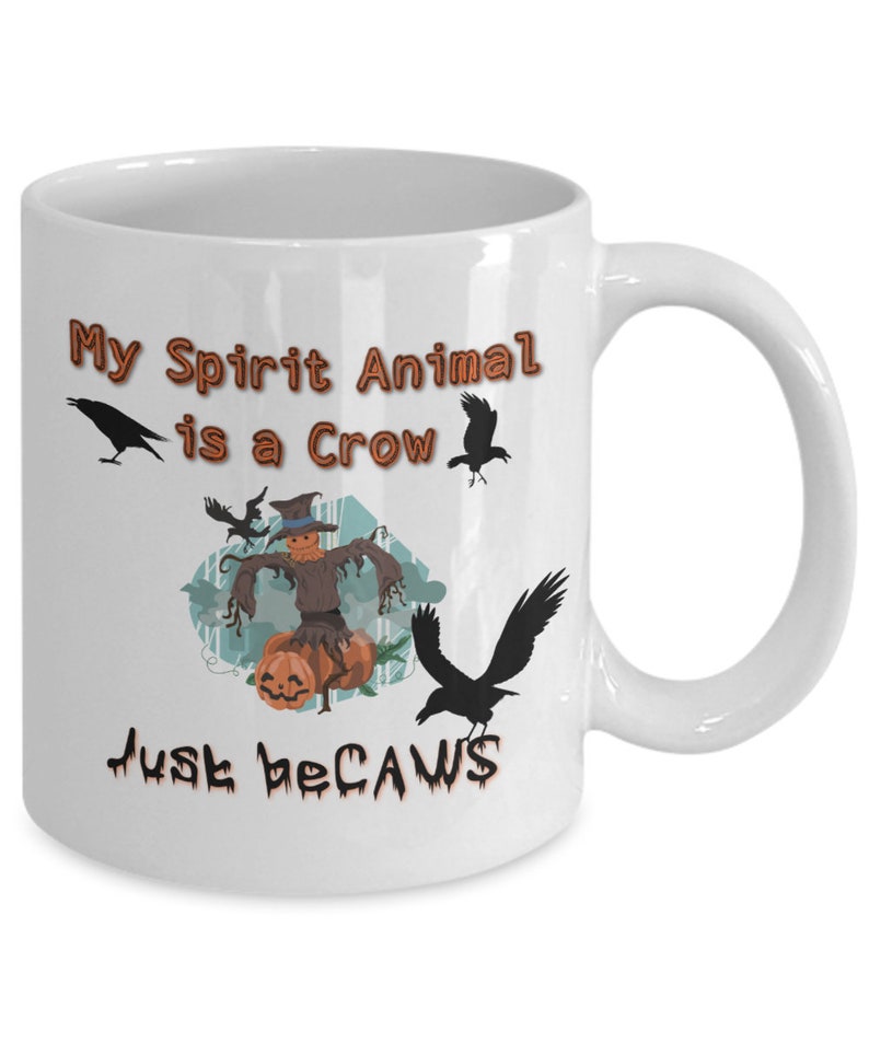 Puede incluir: Taza de caf&eacute; de cer&aacute;mica blanca con un dise&ntilde;o negro y naranja. La taza presenta un espantap&aacute;jaros con calabazas y cuervos. El texto en la taza dice "My Spirit Animal is a Crow Just Because".