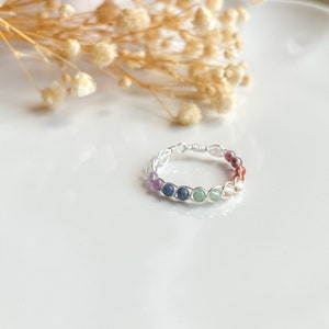 May include: A silver wire wrapped ring with a rainbow of gemstones. The ring features amethyst, sapphire, emerald, peridot, citrine, carnelian, and red jasper.