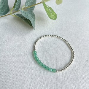 May include: A silver beaded bracelet with a row of light green gemstone beads.