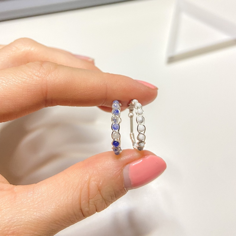 May include: Two silver wire wrapped rings with blue and white beads. The ring on the left has blue beads that fade to white. The ring on the right has white beads.
