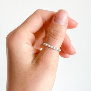 May include: A silver ring with white beads on someone's thumb.