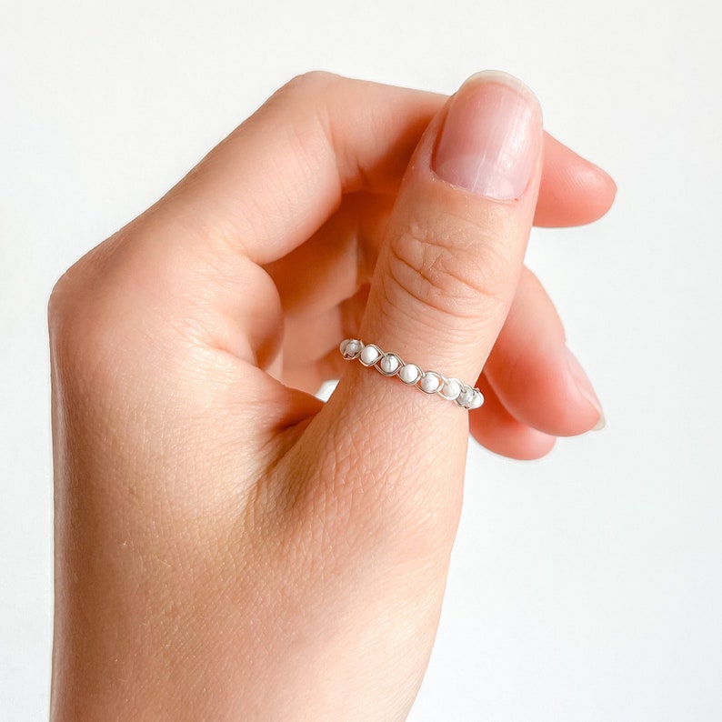 May include: A silver ring with white beads on someone's thumb.