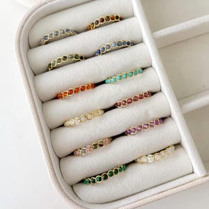 May include: A white jewellery box containing 10 rings in various colours. The rings are made of gold and feature small beads of different colours.